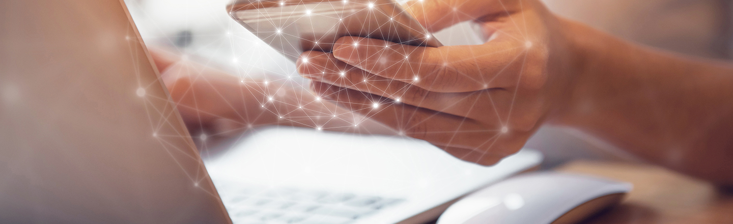 Hands holding a mobile phone and a laptop computer