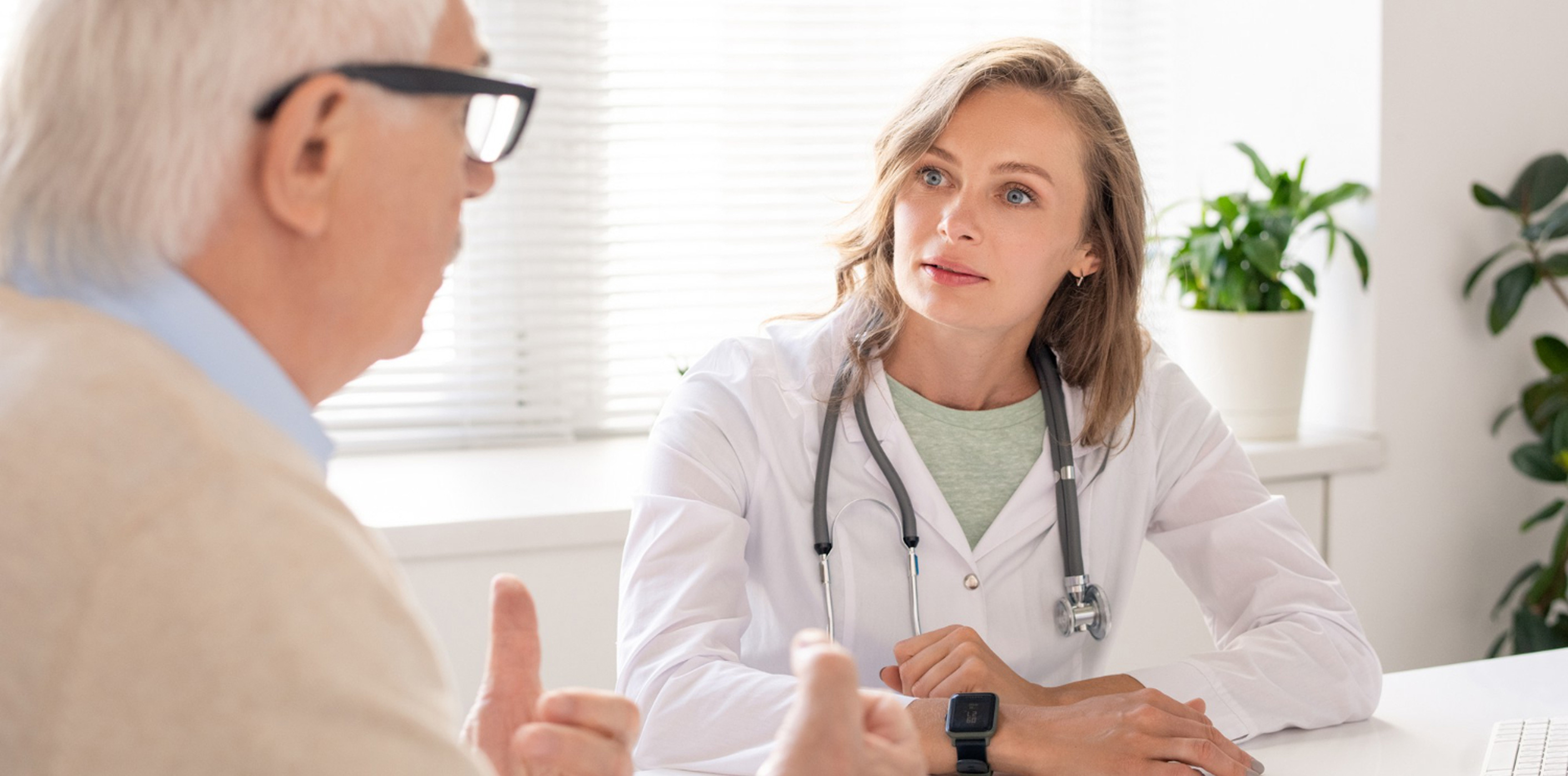 Médecin en consultation avec un patient âgé dans un cabinet; elle écoute attentivement et explique quelque chose.